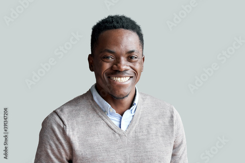 Smiling cheerful young adult african american ethnicity man looking at camera standing at home office background. Happy confident black guy posing for headshot face front close up portrait. photo