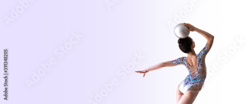 Girl gymnast doing balance exercise with silver ball (back view)
