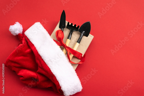 Christmas and new year composition with garden tools, shovel and rake and Santa Claus hat on a red background. The concept of gardening and farming for cards, calendars, covers. photo