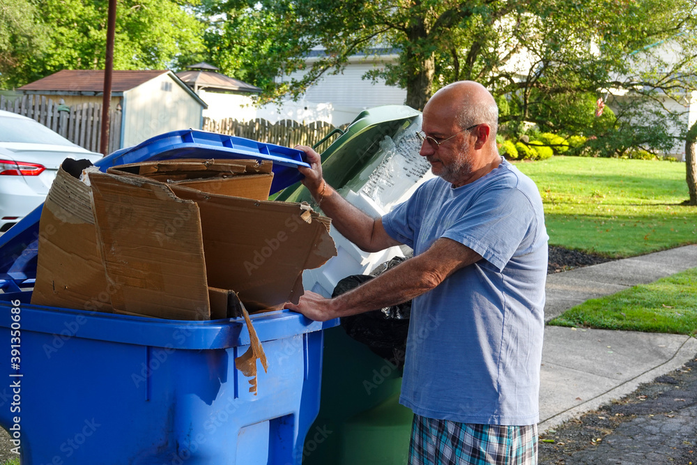 Bald senior citizen man standing in a street with his hand on a full trash can Bald senior citizen man standing in a street with his hand on a full trash can