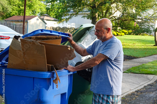 Bald senior citizen man standing in a street with his hand on a full trash can © ALAN