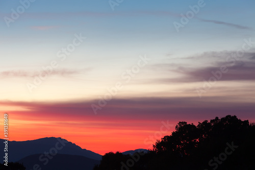 Amazing, vivid colors of a sunset sky and silhouette mountains and trees in the foreground