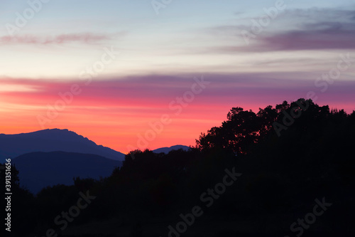 Amazing, vivid colors of a sunset sky and silhouette mountains and trees in the foreground