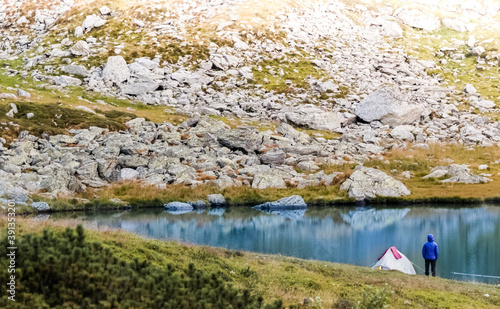 The tourist is standing near the tent. Lake in the Carpathian mountains. Girl in a warm jacket.