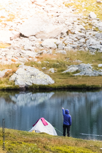 The tourist is standing near the tent. Lake in the Carpathian mountains. Girl in a warm jacket.