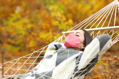 Relaxed woman wearing mask resting on hammock in autumn