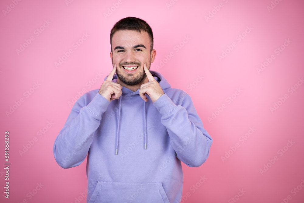 Young handsome man wearing casual sweatshirt over isolated pink background smiling confident showing and pointing with fingers teeth and mouth Young handsome man wearing casual sweatshirt over isolated pink background smiling confident showing and pointing with fingers teeth and mouth