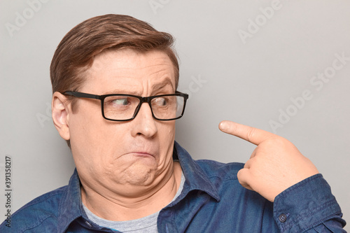 Portrait of funny confused man pointing with index finger at himself