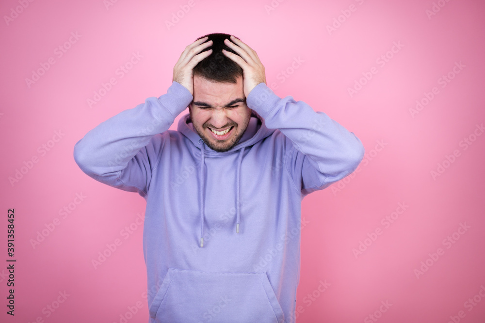Young handsome man wearing casual sweatshirt over isolated pink background suffering from headache desperate and stressed because pain and migraine with her hands on head Young handsome man wearing casual sweatshirt over isolated pink background suffering from headache desperate and stressed because pain and migraine with her hands on head