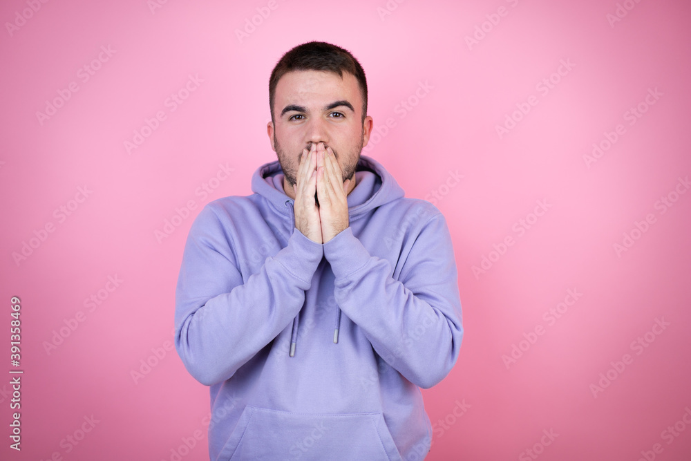 Young handsome man wearing casual sweatshirt over isolated pink background with her hands over her mouth and surprised Young handsome man wearing casual sweatshirt over isolated pink background with her hands over her mouth and surprised