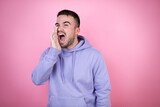 Young handsome man wearing casual sweatshirt over isolated pink background shouting and screaming loud to side with hand on mouth