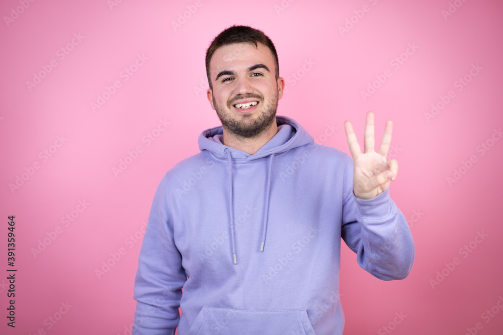 Young handsome man wearing casual sweatshirt over isolated pink background showing and pointing up with fingers number three while smiling confident and happy Young handsome man wearing casual sweatshirt over isolated pink background showing and pointing up with fingers number three while smiling confident and happy
