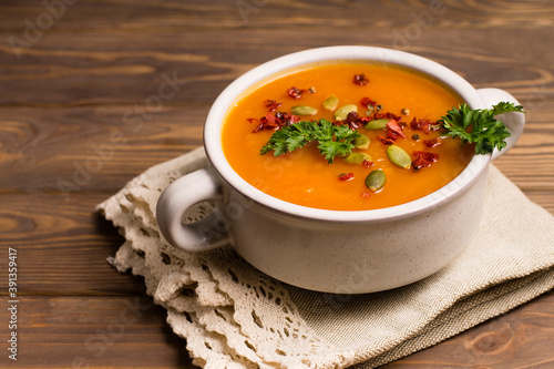 Pumpkin cream soup with herbs and spices, on a wooden background.