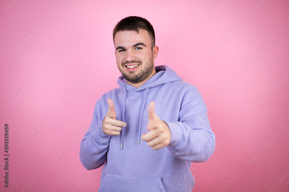 Young handsome man wearing casual sweatshirt over isolated pink background pointing to you and the camera with fingers, smiling positive and cheerful Young handsome man wearing casual sweatshirt over isolated pink background pointing to you and the camera with fingers, smiling positive and cheerful