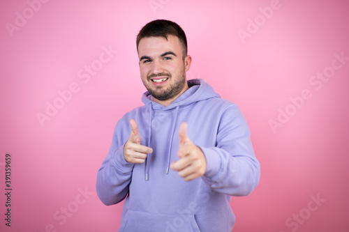 Young handsome man wearing casual sweatshirt over isolated pink background pointing to you and the camera with fingers, smiling positive and cheerful © Irene