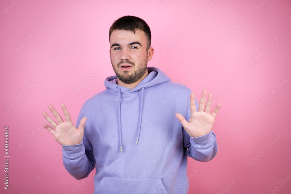 Young handsome man wearing casual sweatshirt over isolated pink background afraid and terrified with fear expression stop gesture with hands, shouting in shock. Panic concept Young handsome man wearing casual sweatshirt over isolated pink background afraid and terrified with fear expression stop gesture with hands, shouting in shock. Panic concept