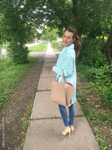 Stylish woman in mint oversize coat with beige purse or handbag posing on the street. Trendy outfit. Look of the day.