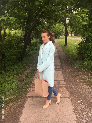 Stylish woman in mint oversize coat with beige purse or handbag posing on the street. Trendy outfit. Look of the day.