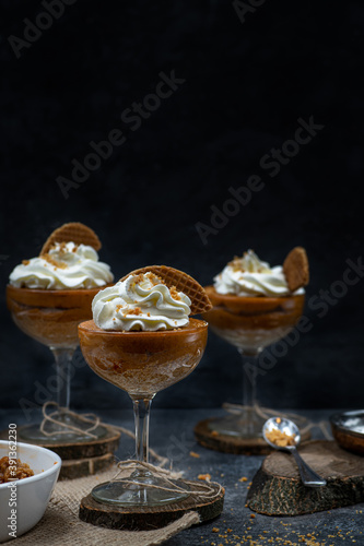 Pumpkin mousse and whipped cream served in tall glasses against black background, copy space