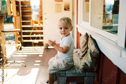 Little blonde boy with cup of water in his hands sitting on a wooden bench photo