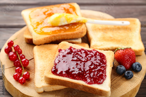 Toasts with jam and ripe berries on wooden table