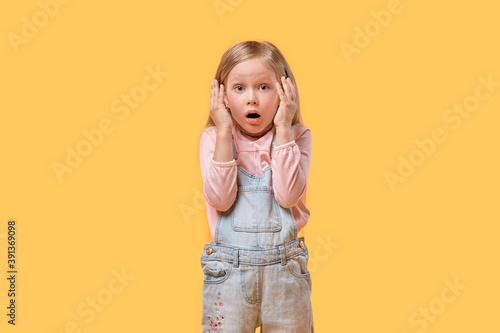 A small blonde girl with a surprised face looks at the camera. Yellow isolated background.
