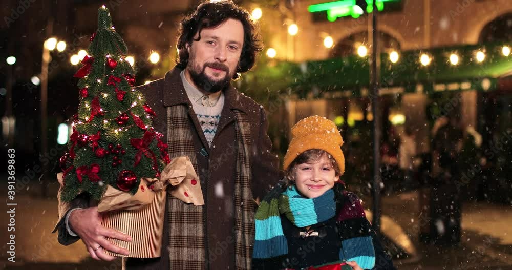 Portrait of happy Caucasian family outdoors with presents while snowing. Loving father with cute teen boy standing in decorated city on christmas eve with xmas gifts in hands. Winter holidays concept