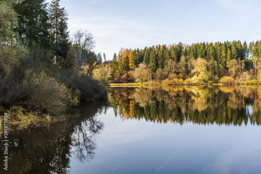 Autumn leaves are reflected in the water of the Windach reservoir in Bavaria