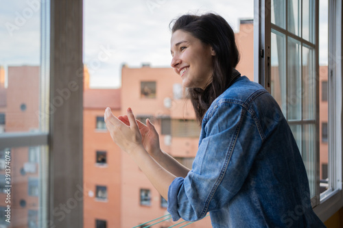 Young Woman Applauding From The Window During Coronavirus Lockdown.