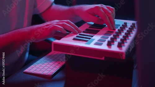 Male hands recording music, playing electronic keyboard, midi keys on the table with neon lights. Closeup of male hands composing music in night using midi controller photo