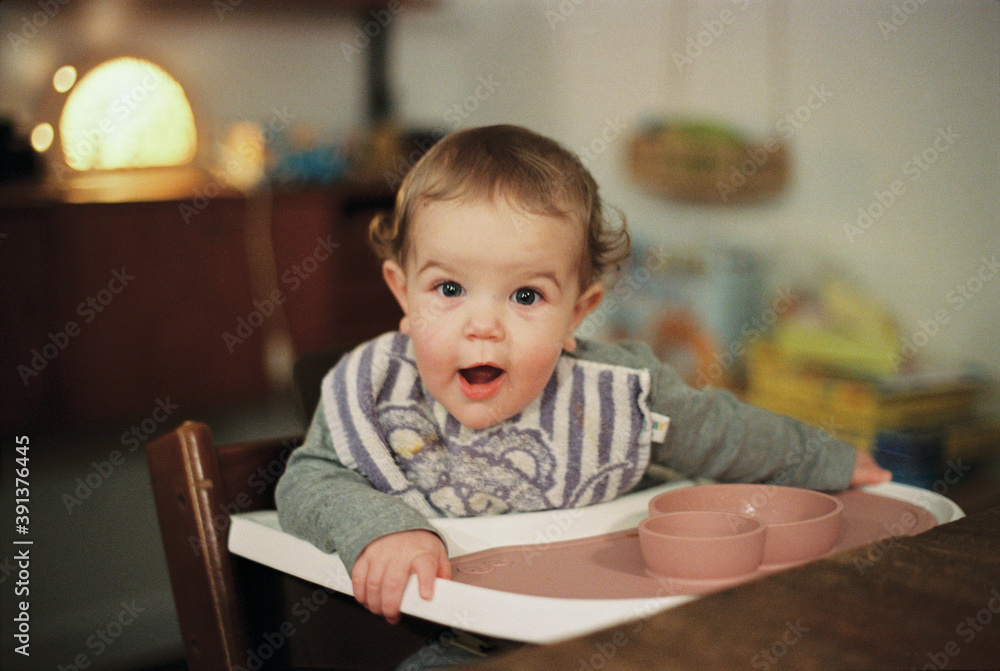 Girl sitting in a wooden high chair with food tablet looking surprised and happy at the camera Girl sitting in a wooden high chair with food tablet looking surprised and happy at the camera