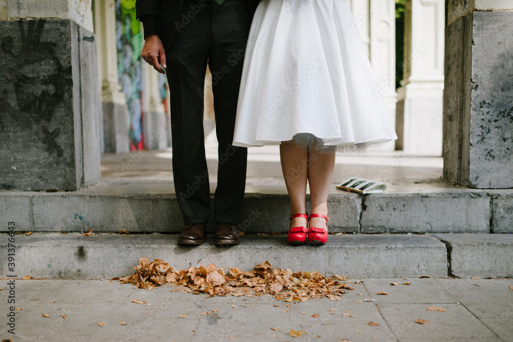 bride with bright red shoes with bow standing next to groom dressed in black with brow shoes bride with bright red shoes with bow standing next to groom dressed in black with brow shoes