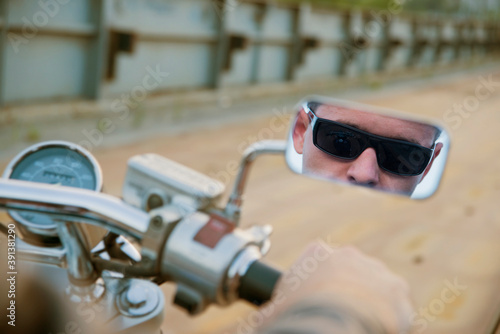 Unregnizable person Reflection image on mirror Biker man sits on bike and wearing black sunglasses On metal bridge background in perspective Empty copy space for inscrption Hand on the steering wheel photo