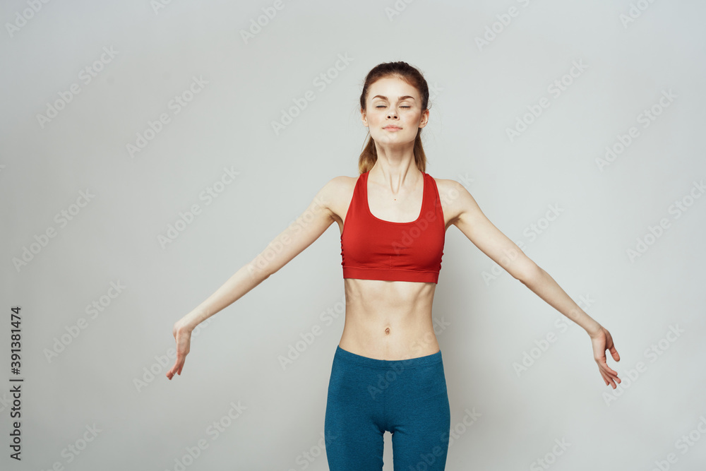 A woman in a red T-shirt on a light background is engaged in fitness gestures with her hands a slim figure A woman in a red T-shirt on a light background is engaged in fitness gestures with her hands a slim figure