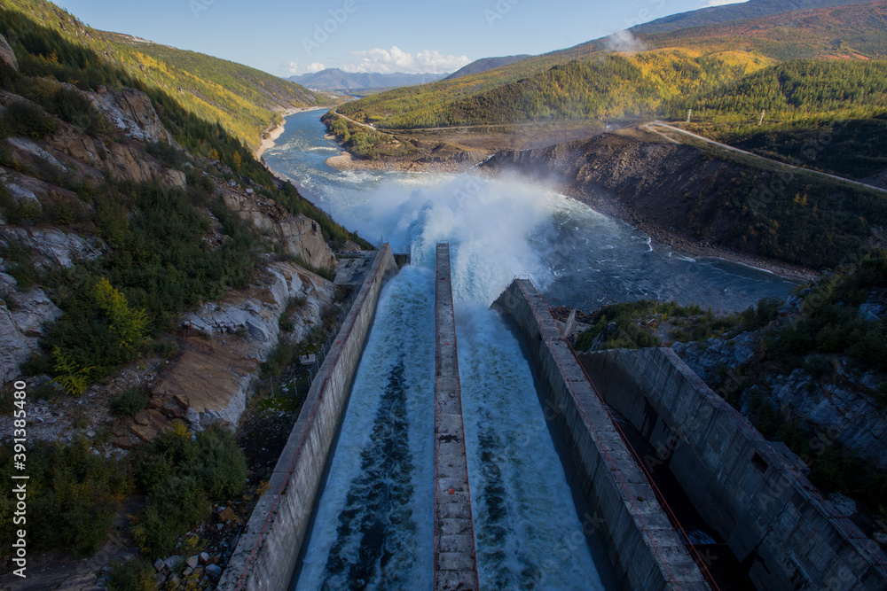 Kolyma hydroelectric power station in Magadan region, Russia. Spillway from the dam of the hydroelectric power station. A huge stream of water flows into the river against the background of high hills