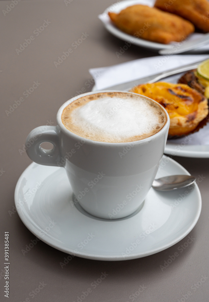 Cup of cappuccino coffee served with traditional dessert pastry in Portugal, nata eggs cream cakes with fruits Cup of cappuccino coffee served with traditional dessert pastry in Portugal, nata eggs cream cakes with fruits