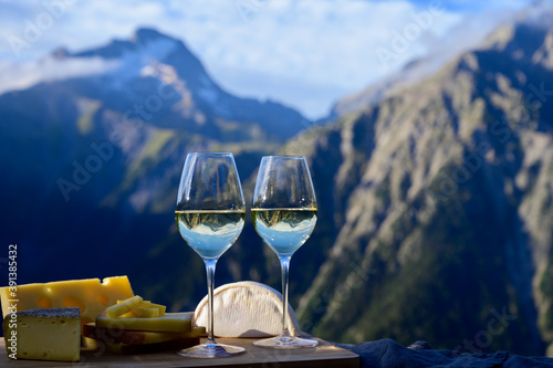 Tasty cheese and wine from Savoy region in France, beaufort, abondance, emmental, tomme and reblochon de savoie cheeses and glass of white wine served outdoor with Alpine mountains peaks on background photo