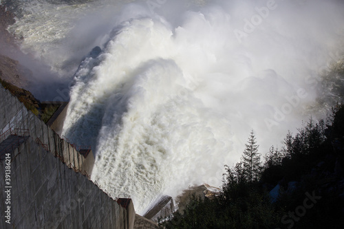 Kolyma hydroelectric power station in Magadan region, Russia. Spillway from the dam of the hydroelectric power station. A huge stream of water flows into the river against the background of high hills photo