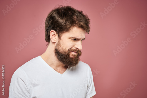 Emotional bearded man in white T-shirt discontent pink background