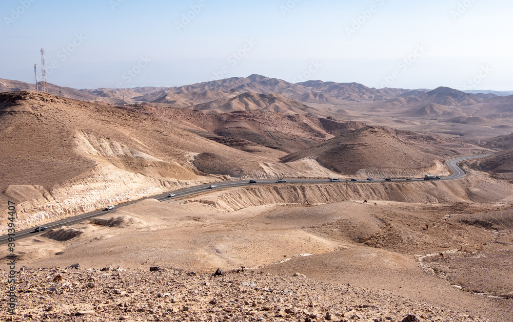 Bird eye view on serpentine road 31 descending from city Arad to the Dead Sea, Judaean Desert, Israel. Panoramic landscape of the desert around the road. Cars on the road. City Arad on the background. Bird eye view on serpentine road 31 descending from city Arad to the Dead Sea, Judaean Desert, Israel. Panoramic landscape of the desert around the road. Cars on the road. City Arad on the background.