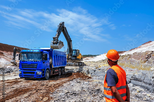 worker looks at the process of loading clay. excavator extracts clay and loads into blue truck. Clay mining.