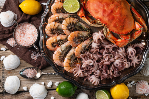 Close-up view of dish with assorted seafood. Cooked crab, baby octopuses and tiger shrimps served with ice cubes, lime and seashells on rustic wooden background. Seafood concept. View from above.