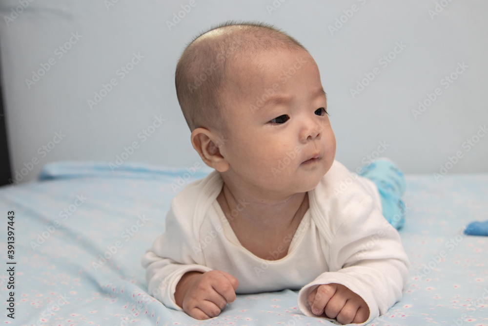 Happy smiling face of Chinese baby boy on tummy time on bed. Newborn child relaxing in bed Happy smiling face of Chinese baby boy on tummy time on bed. Newborn child relaxing in bed