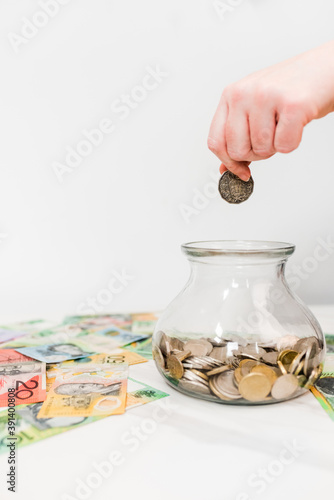 Vertical shot of a hand putting a coin in the jar on the white background with Australian dollars photo