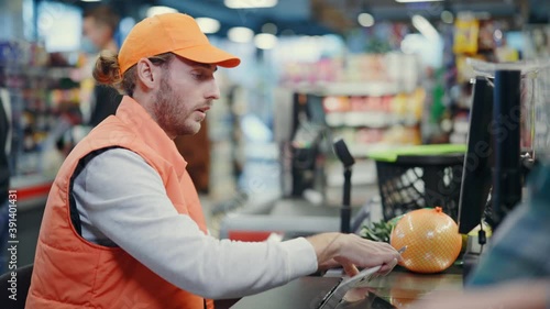 Sleepy tired bearded male cashier incompetent worker talking indifferent with customer being rude scanning items too fast. Bad wservices. Supermarket.