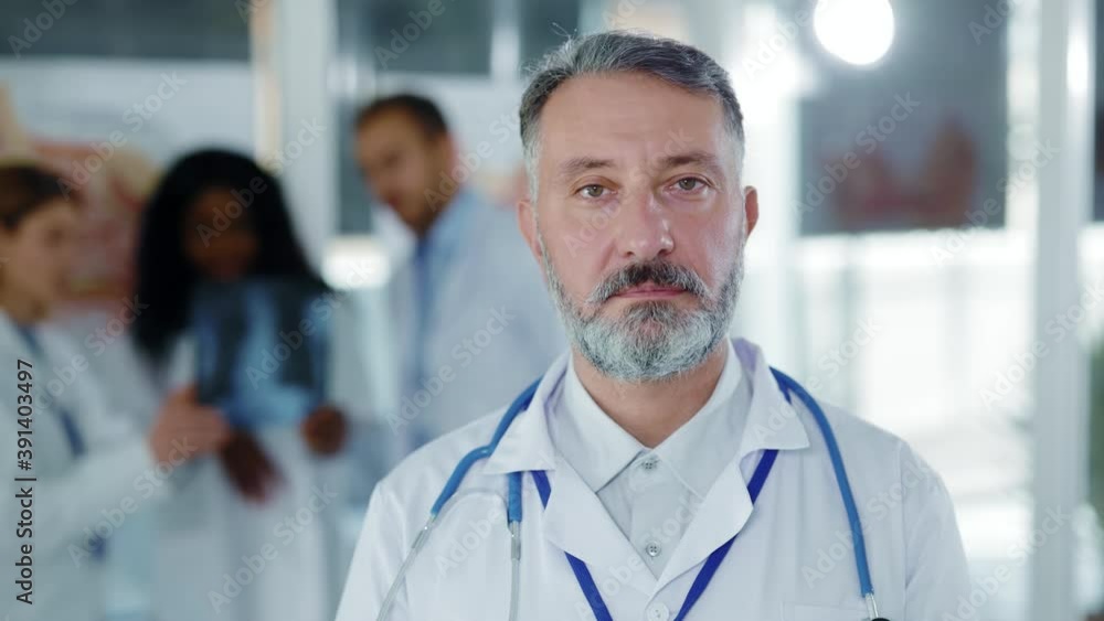 Portrait of attractive middle aged senior caucasian doctor in medical office wearing stethoscope on neck collaborating with colleagues meeting at hospital. Portrait of attractive middle aged senior caucasian doctor in medical office wearing stethoscope on neck collaborating with colleagues meeting at hospital.