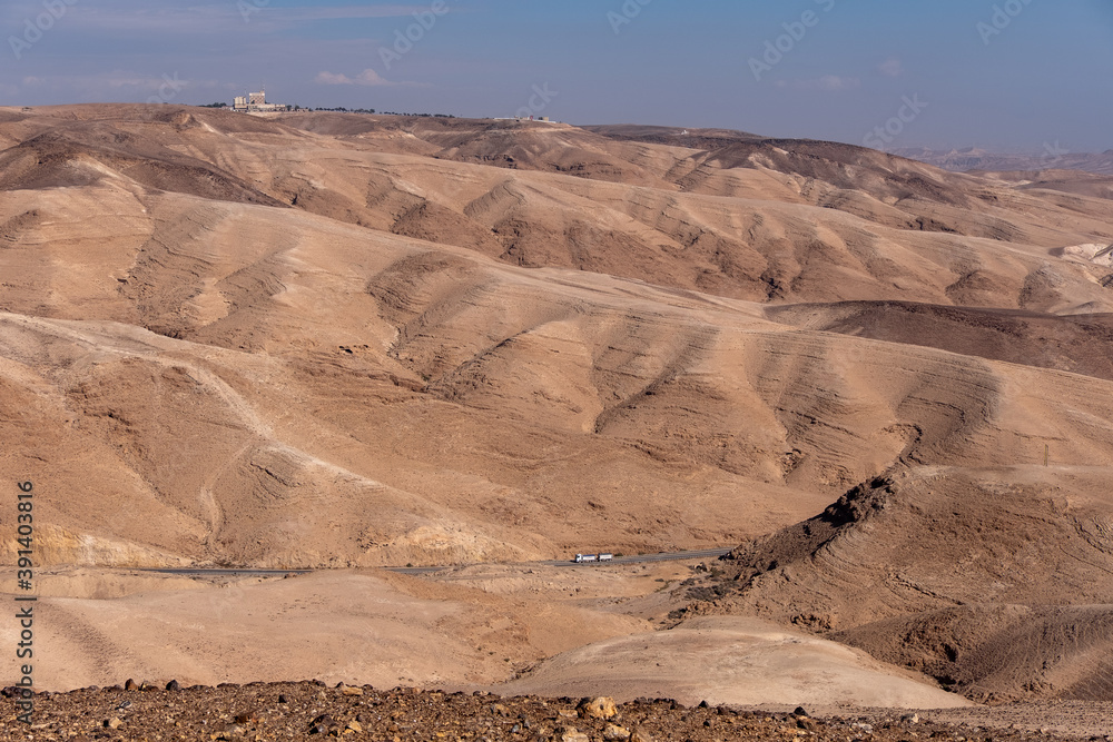 Bird eye view on a road number 31 descending from city Arad to the Dead Sea, Judaean Desert, Israel. Panoramic landscape of the desert with sandy hills around the road. Big truck on the road.