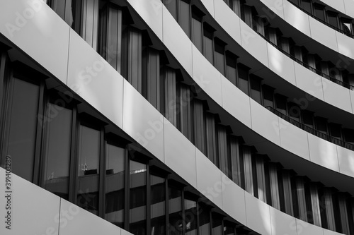 Black and white tone, close-up and detail of exterior curvature facade with contrast colour material of black windows and white aluminium panels in wavy shape.