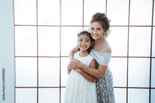Portrait of a happy mother hugging her happy daughter. Familiy photo concept, standing by the window