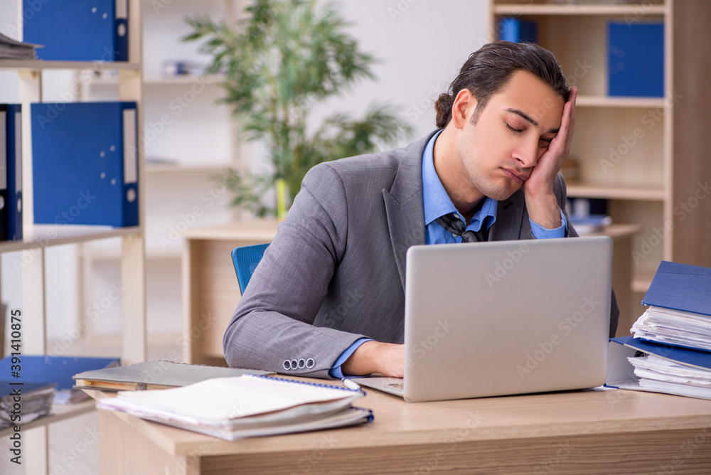 Fototapeta premium Young businessman employee unhappy with excessive work in the o